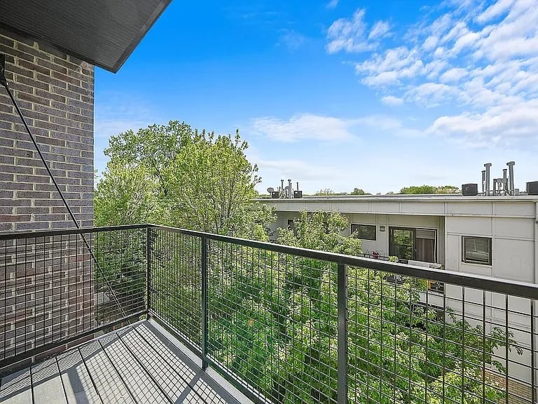 Modern apartment balcony with metal railing overlooking green trees and urban skyline on a clear blue sky day