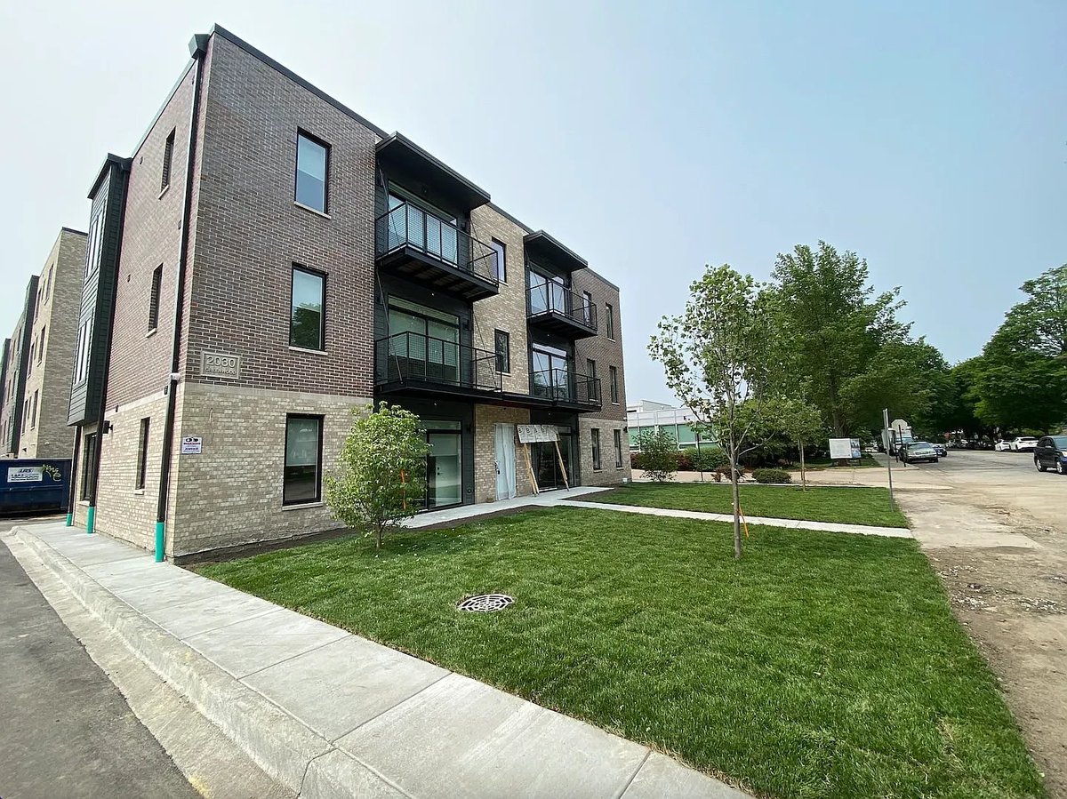 Modern multi-story apartment building with brick facade, black balconies, and manicured green lawn