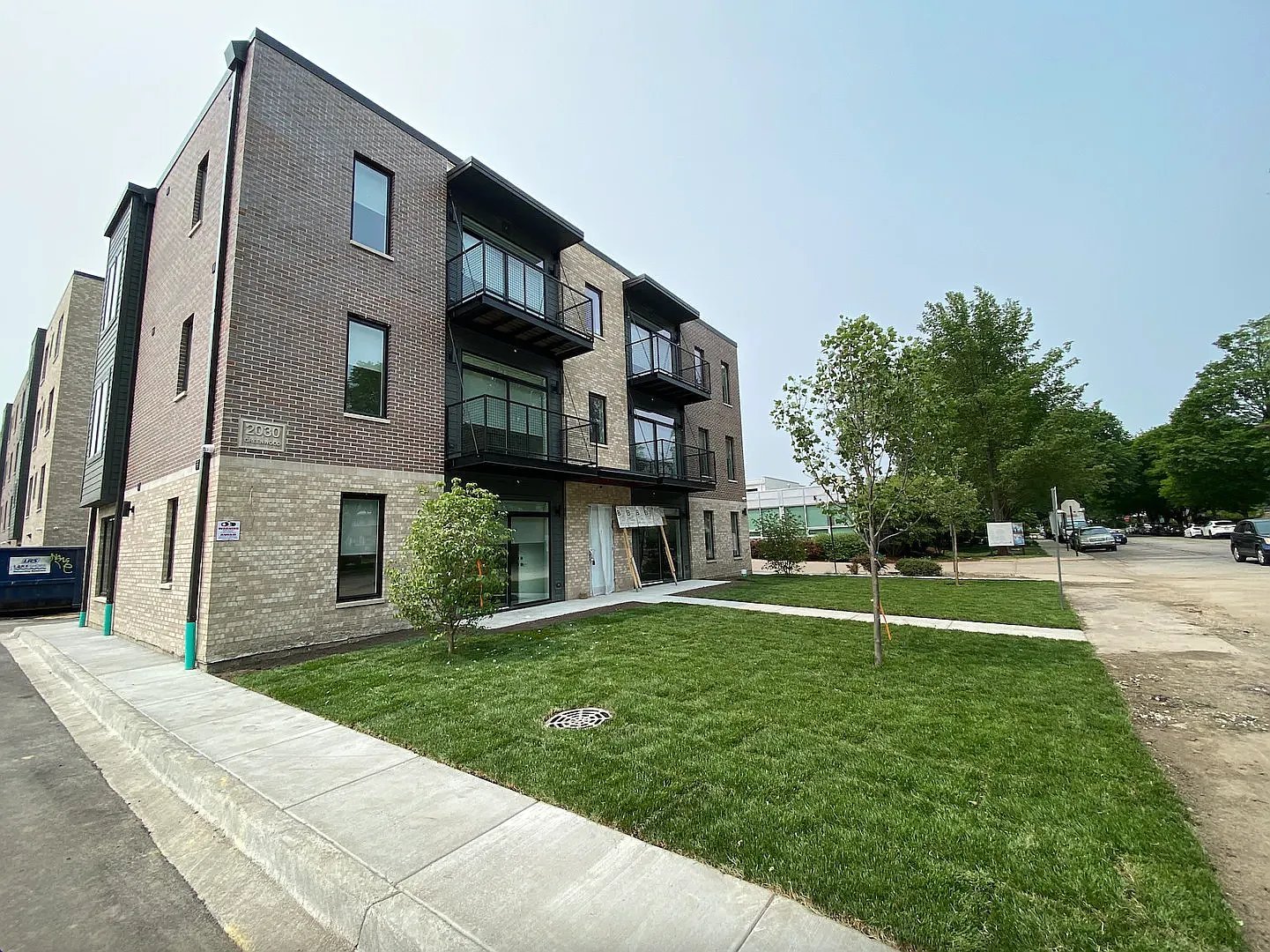 Modern multi-story apartment building with brick facade, black balconies, and manicured green lawn