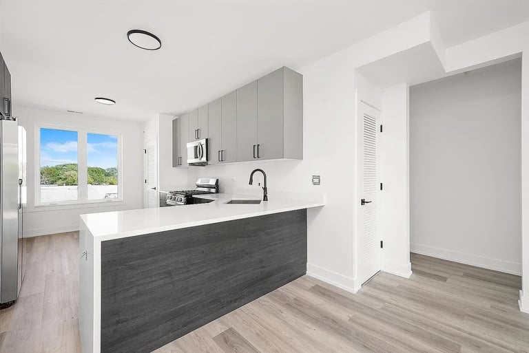 Modern kitchen with white cabinetry, dark waterfall island countertop, stainless steel appliances, and light wood flooring